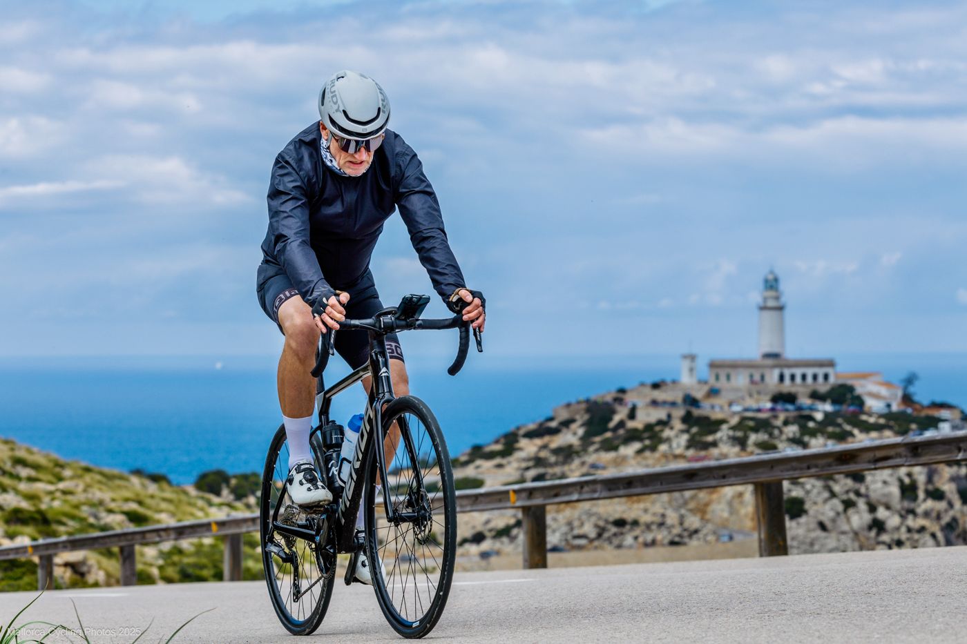 Harald fährt eine Küstenstraße hinauf, im Hintergrund der Leuchtturm am Meer